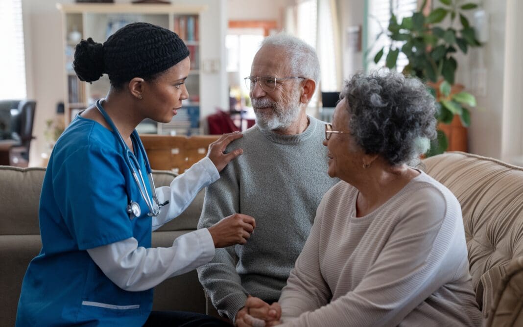 Nurse consulting with elderly veteran and spouse about VA caregiver stipend calculator support at home.